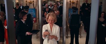 Movie still from “RED” (2010), directed by Robert Schwentke – An older woman holding a cell phone in front of a group of people; Medium shot, Low angle