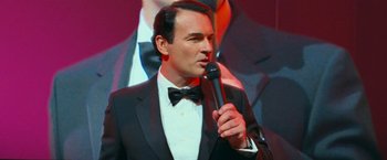 Movie still from “RED” (2010), directed by Robert Schwentke – A man in a tuxedo is holding a microphone; Close Up shot, High angle