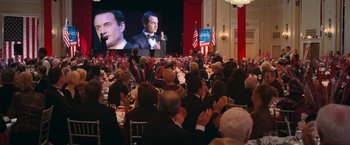 Movie still from “RED” (2010), directed by Robert Schwentke – A crowd of people sitting at tables in front of a large screen; Medium shot, High angle