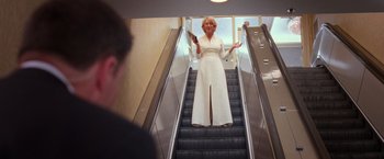 Movie still from “RED” (2010), directed by Robert Schwentke – A woman in a long white dress standing on an escalator; Wide shot, Low angle