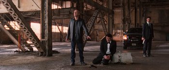 Movie still from “RED” (2010), directed by Robert Schwentke – Two men in suits are standing in a warehouse; Wide shot, Low angle