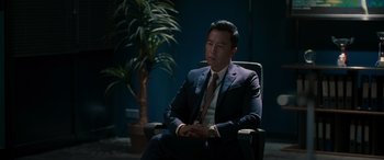Movie still from “Raging Fire” (2021), directed by Benny Chan – A man in a suit and tie sitting in a chair in a room; Medium shot, Over the shoulder angle