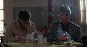 Movie still from “Rain Man” (1988), directed by Barry Levinson – Two people sitting at a table with papers and a cigarette; Medium shot, Over the shoulder angle