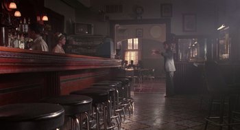 Movie still from “Rain Man” (1988), directed by Barry Levinson – A man is standing at a bar with a bunch of stools in front of him; Wide shot, Over the shoulder angle