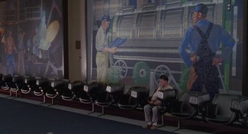 Movie still from “Rain Man” (1988), directed by Barry Levinson – A man sitting in a row of seats in front of a mural; Wide shot, High angle