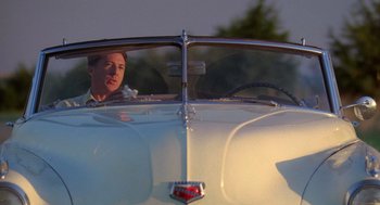 Movie still from “Rain Man” (1988), directed by Barry Levinson – A man driving a classic car in the sunlight; Medium shot, Over the shoulder angle