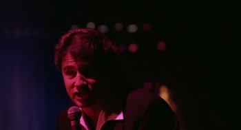 Movie still from “Rain Man” (1988), directed by Barry Levinson – A man in a suit is speaking into a microphone in front of a crowd; Close Up shot, Low angle