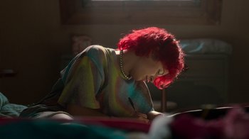 Movie still from “Rainbow” (2022), directed by Paco León – A woman with red hair writing on a piece of paper; Medium shot, High angle