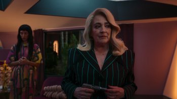 Movie still from “Rainbow” (2022), directed by Paco León – A woman holding a cell phone while standing in a room; Medium shot, Over the shoulder angle