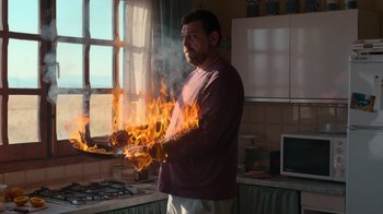 Movie still from “Rainbow” (2022), directed by Paco León – A man is holding fire in a kitchen; Medium shot, Low angle