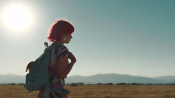 Movie still from “Rainbow” (2022), directed by Paco León – A woman with a backpack standing in the middle of an open field; Wide shot, Low angle