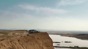 Movie still from “Rainbow” (2022), directed by Paco León – A car driving on top of a cliff next to a body of water; Extreme Wide shot, Low angle