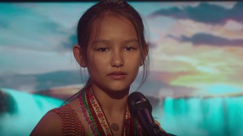 Movie still from “Rainbow” (2022), directed by Paco León – A young girl is holding a microphone in her hand; Close Up shot, Over the shoulder angle