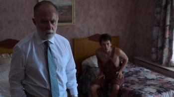 Movie still from “Rainbow” (2022), directed by Paco León – A man sitting on a bed next to another man in front of a bed; Medium shot, Over the shoulder angle