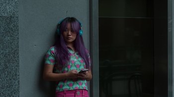 Movie still from “Rainbow” (2022), directed by Paco León – A woman with purple hair wearing headphones and holding a cell phone; Medium shot, High angle