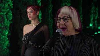 Movie still from “Rainbow” (2022), directed by Paco León – A woman with pink hair is speaking into a microphone; Close Up shot, Over the shoulder angle