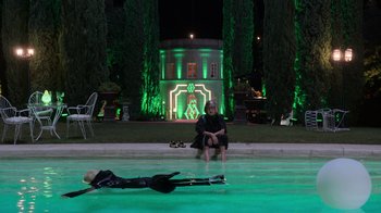 Movie still from “Rainbow” (2022), directed by Paco León – A woman sitting on the edge of a swimming pool; Wide shot, High angle