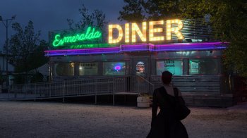 Movie still from “Rainbow” (2022), directed by Paco León – A woman standing in front of a diner at night; Extreme Wide shot, Low angle