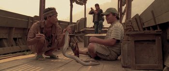 Movie still from “Rambo” (2008), directed by Sylvester Stallone – Two men sitting on the ground holding a snake; Medium shot, Low angle