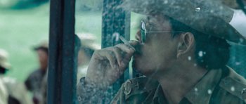 Movie still from “Rambo” (2008), directed by Sylvester Stallone – A man smoking a cigarette while looking out a window; Close Up shot, Over the shoulder angle