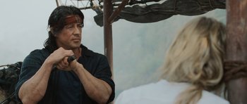 Movie still from “Rambo” (2008), directed by Sylvester Stallone – A man holding an umbrella while standing next to a woman; Close Up shot, Over the shoulder angle