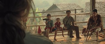 Movie still from “Rambo” (2008), directed by Sylvester Stallone – A group of people sitting on top of a wooden bench; Wide shot, Over the shoulder angle