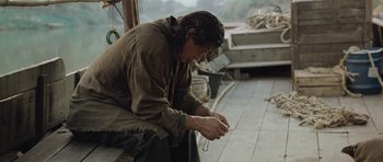 Movie still from “Rambo” (2008), directed by Sylvester Stallone – A man sitting on the ground with a string in his hand; Medium shot, High angle