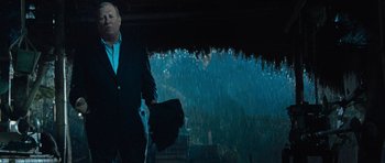 Movie still from “Rambo” (2008), directed by Sylvester Stallone – A man in a black suit holding a black bag in the rain; Medium shot, Low angle