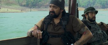 Movie still from “Rambo” (2008), directed by Sylvester Stallone – A man with a beard wearing a black hat and holding a knife; Medium shot, Over the shoulder angle