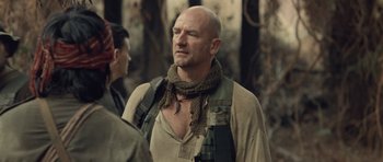 Movie still from “Rambo” (2008), directed by Sylvester Stallone – A bald man with a scarf around his neck; Close Up shot, Over the shoulder angle