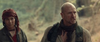 Movie still from “Rambo” (2008), directed by Sylvester Stallone – A bald man with a beard and a scarf around his neck; Close Up shot, Over the shoulder angle