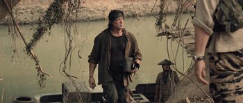 Movie still from “Rambo” (2008), directed by Sylvester Stallone – A man holding a bucket while standing next to a river; Medium shot, Low angle
