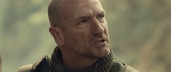 Movie still from “Rambo” (2008), directed by Sylvester Stallone – A man with a bald head wearing a scarf looking to his left; Close Up shot, Low angle