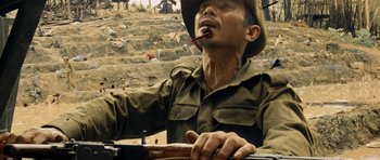 Movie still from “Rambo” (2008), directed by Sylvester Stallone – A man in a hat is holding a rifle and smoking; Close Up shot, High angle