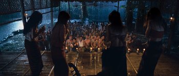 Movie still from “Rambo” (2008), directed by Sylvester Stallone – A group of people sitting in front of a stage; Wide shot, High angle