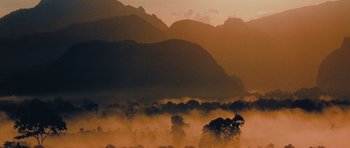 Movie still from “Rambo” (2008), directed by Sylvester Stallone – The sun is setting over the mountains with trees in the foreground; Extreme Wide shot, Low angle