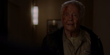 Movie still from “Ray Donovan: The Movie” (2022), directed by David Hollander – An old man with a knife in his mouth; Close Up shot, Over the shoulder angle