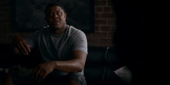 Movie still from “Ray Donovan: The Movie” (2022), directed by David Hollander – A man sitting on a couch in front of a brick wall; Medium shot, Over the shoulder angle