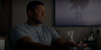 Movie still from “Ray Donovan: The Movie” (2022), directed by David Hollander – A man sitting at a table in front of a painting; Medium shot, Over the shoulder angle