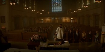 Movie still from “Ray Donovan: The Movie” (2022), directed by David Hollander – A priest standing in front of people in a church; Extreme Wide shot, High angle