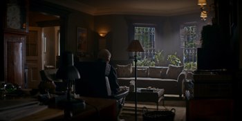 Movie still from “Ray Donovan: The Movie” (2022), directed by David Hollander – A man sitting in a chair in a living room; Wide shot, Over the shoulder angle