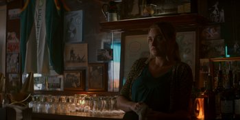 Movie still from “Ray Donovan: The Movie” (2022), directed by David Hollander – A woman sitting at a bar looking at the camera; Medium shot, Over the shoulder angle