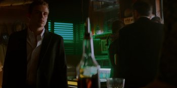 Movie still from “Ray Donovan: The Movie” (2022), directed by David Hollander – A man in a suit and tie in front of a bottle of alcohol; Medium shot, Low angle