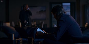 Movie still from “Ray Donovan: The Movie” (2022), directed by David Hollander – Two men sitting in a living room at night looking at a tablet; Medium shot, Over the shoulder angle