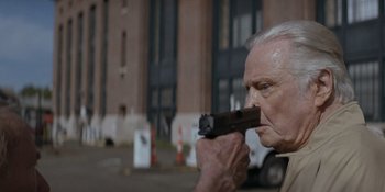 Movie still from “Ray Donovan: The Movie” (2022), directed by David Hollander – An older man holding a gun up to his face; Close Up shot, Over the shoulder angle