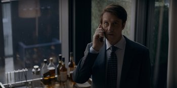 Movie still from “Ray Donovan: The Movie” (2022), directed by David Hollander – A man talking on a cell phone in front of some bottles; Medium shot, Low angle