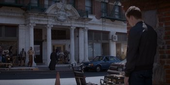 Movie still from “Ray Donovan: The Movie” (2022), directed by David Hollander – A car parked on the side of the road near a building; Wide shot, Over the shoulder angle