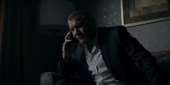 Movie still from “Ray Donovan: The Movie” (2022), directed by David Hollander – A man in a black suit talking on a cell phone; Close Up shot, Low angle