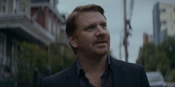 Movie still from “Ray Donovan: The Movie” (2022), directed by David Hollander – A person wearing a suit and tie; Close Up shot, Over the shoulder angle