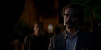 Movie still from “Ray Donovan: The Movie” (2022), directed by David Hollander – A man in a suit and tie standing next to another man in a suit and tie; Close Up shot, Over the shoulder angle